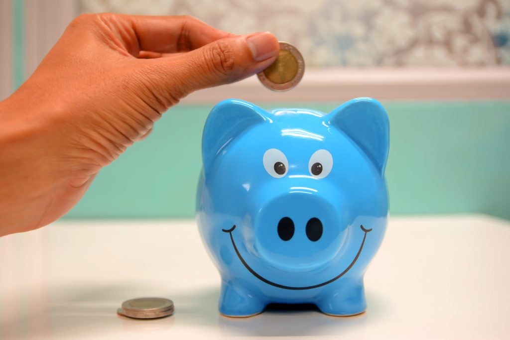 Putting money into a blue piggy bank to support your travel budget.